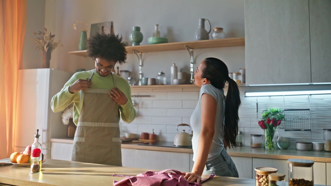 Young man apron cleaning kitchen. Multiracial couple sharing housework home.