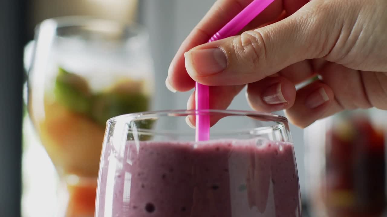 Mano suspendida, alcanzando y doblando una pajita rosa en un vaso de batido morado en el mostrador para beber.