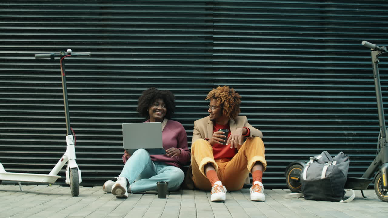 African American Friends Using Laptop and Talking while Sitting on Street