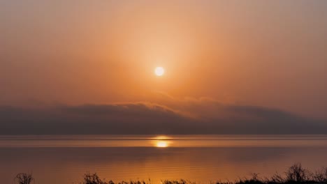 sun rises across orange haze cloud sky above calm lake below, stunning time lapse