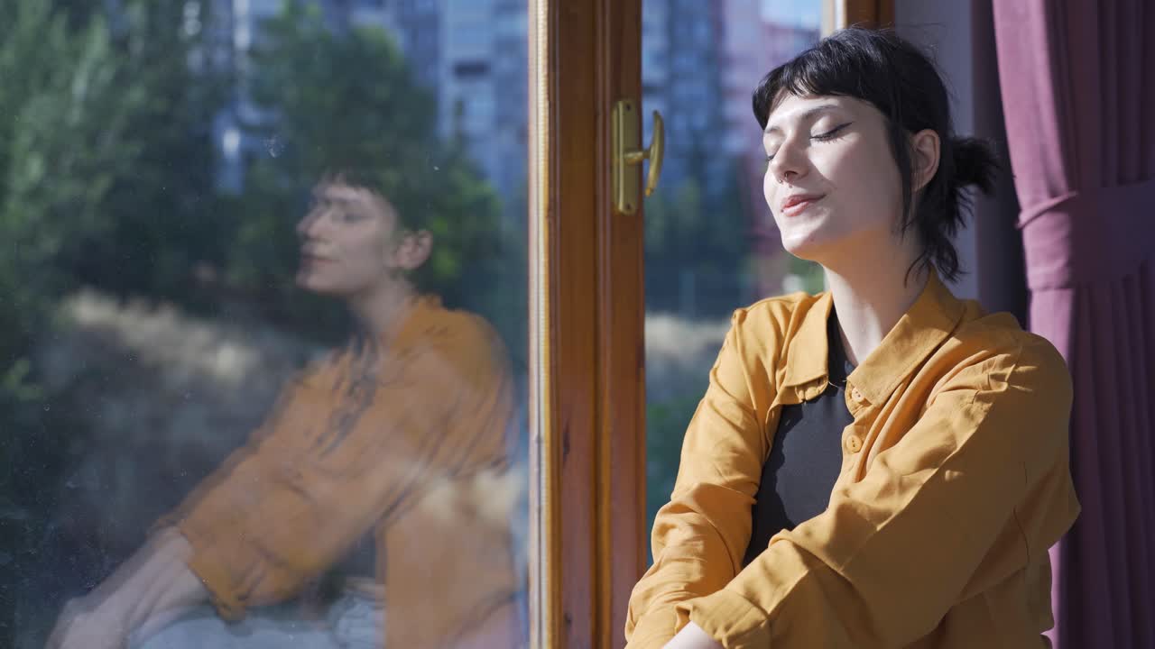 행복한 젊은 여자는 창문 밖을 바라보고 깊은 숨을 쉬고 있습니다.