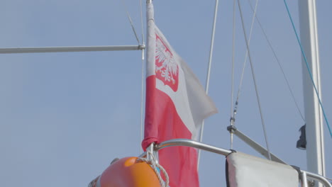 polish flag with the emblem flies in the wind attached to a metal railing on the ship