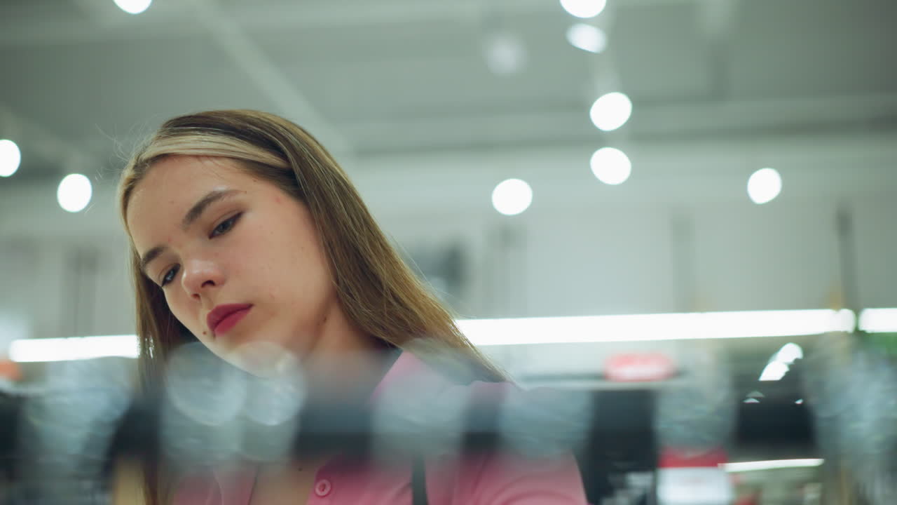 핑크 을 입은 하 여자가 잘 조명된 쇼핑몰에서 움직이고, 그녀의 앞에 있는 무언가에 깊이 초점을 맞추고, 그녀의 앞의 시야는 흐릿하지만 배경은 흐릿한 빛에 의해 조명됩니다.
