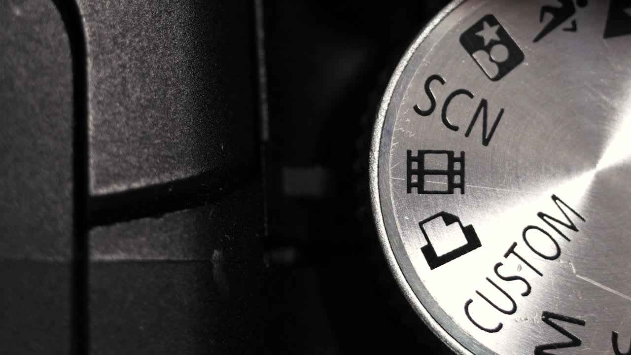 Top down close up of silver mode dial turning on black bridge camera body