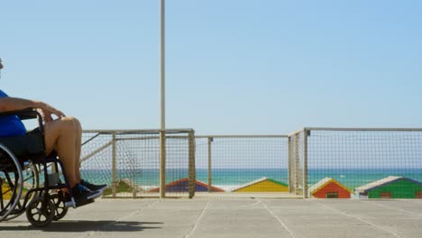 Side-view-of-active-senior-Caucasian-woman-pushing-senior-man-on-wheelchair-at-beach-4k