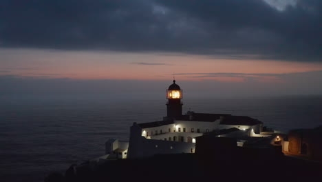 Amazing-aerial-drone-circling-around-beautiful-lighthouse-in-Lagos-Algarve-Portugal,-sunset-dusk