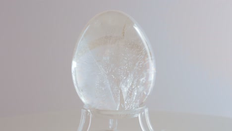 clear quarts crystal mineral egg rotating on a turn table in front of a white background