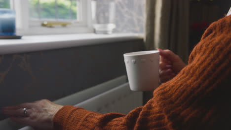 Senior-Woman-In-Wheelchair-Trying-To-Keep-Warm-By-Radiator-During-Cost-Of-Living-Energy-Crisis