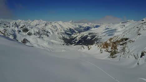 Drone-flying-over-skintrack-towards-vast-empty-mountain-valley-in-winter