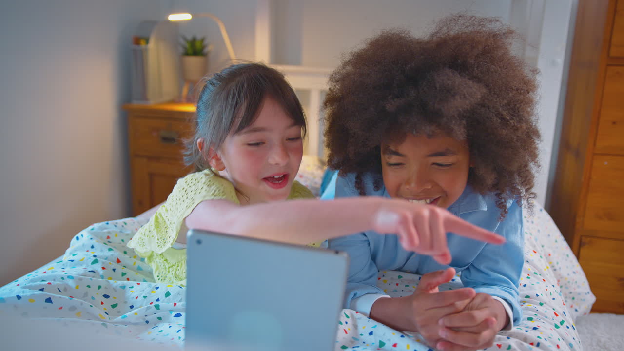 Menina e menino no quarto deitados na cama usando um tablet.