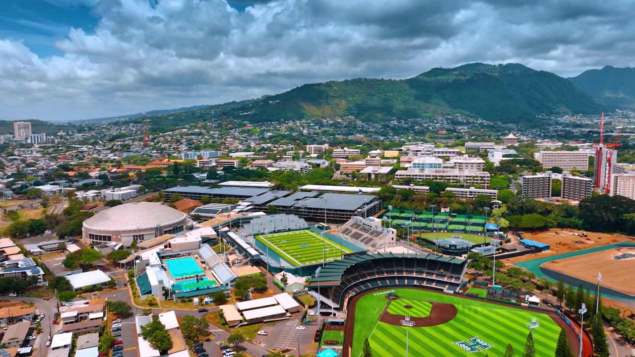 Stadien und Schwimmbad auf dem Gelände der University of Hawaii, Honolulu, Insel Oahu. Grüne Berge vor grauer Wolkenlandschaft im Hintergrund. Luftperspektive