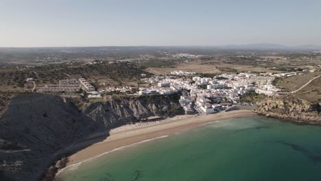 Burgau-Beach-surrounded-by-rocky-cliffs,-calm-emerald-Atlantic-ocean