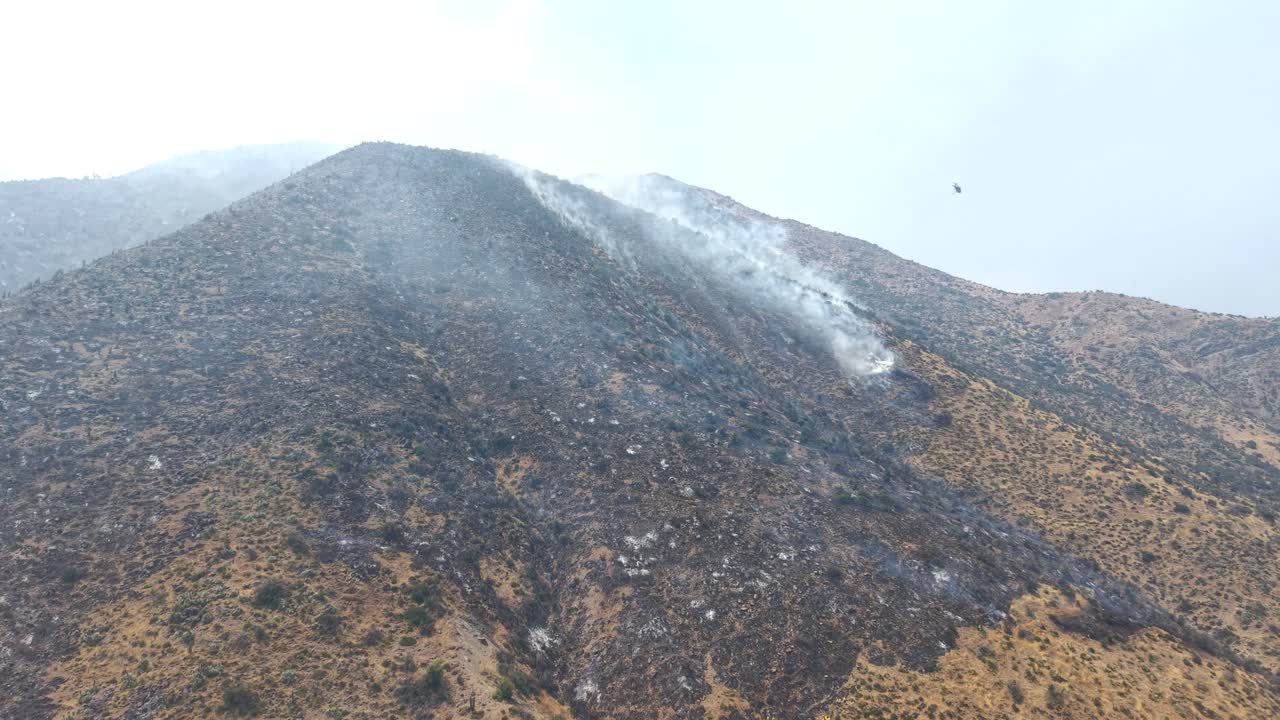 Cinematic aerial drone view of a firefighting airplane performing a water drop on a burnt mountain ridge to extinguish hotspots in the Andes, Chile, 4K