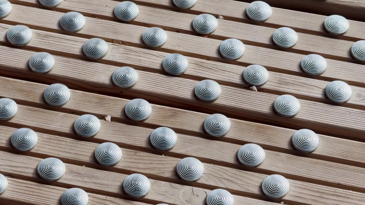 Nærbilde av taktile metallknotter på en gangvei av trelameller, som viser en overflate for tilgjengelighetsveiledning, sklisikker tekstur og en designdetalj for offentlige fotgjengere.