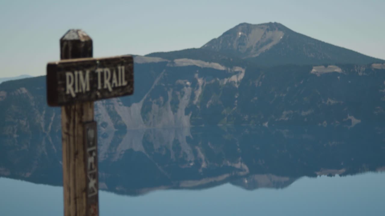 el estante de la señal del comienzo del sendero se enfoca en el lago y las montañas en el fondo.