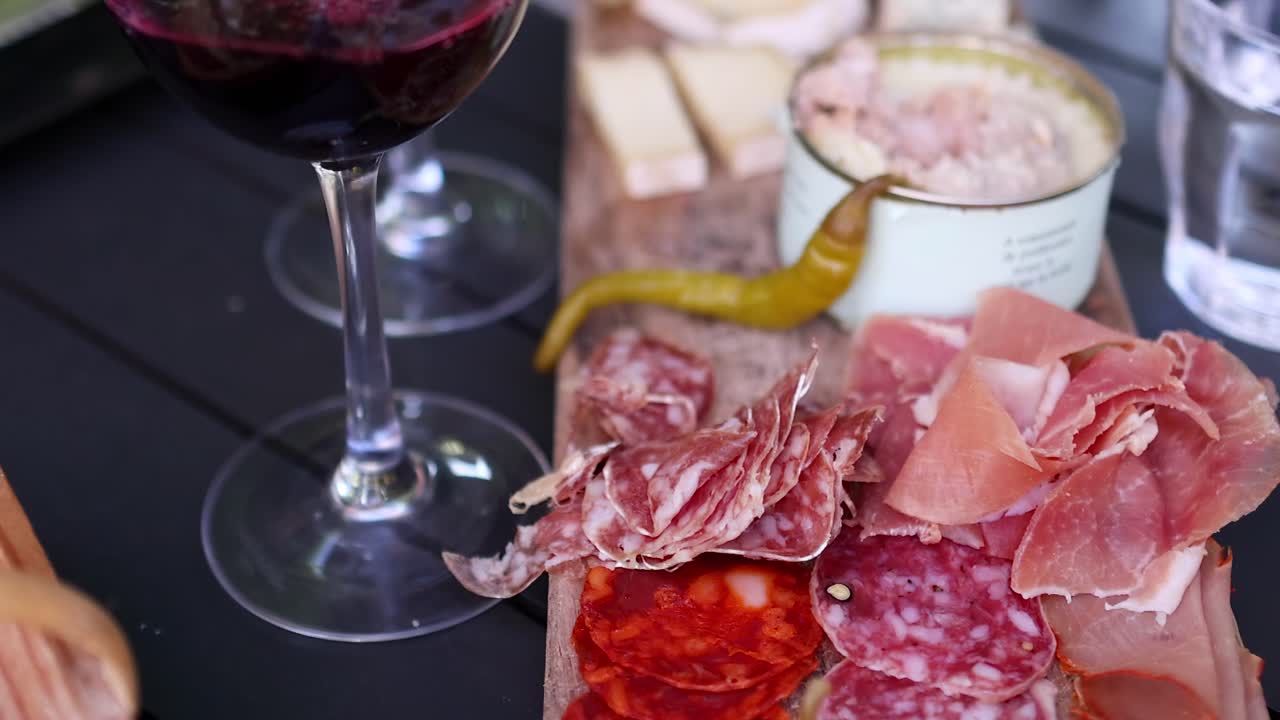 A close-up of assorted meats and a glass of red wine on a black table.