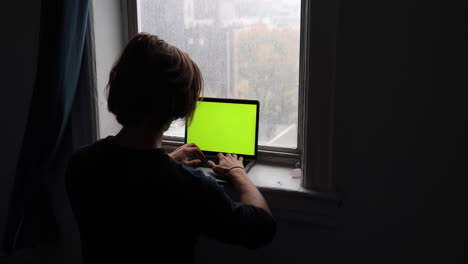 el joven escribe y trabaja en su computadora portátil frente a una hermosa vista de la ventana