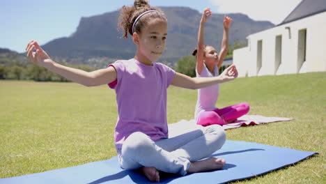 two biracial girls are practicing yoga outdoors on a sunny day in school