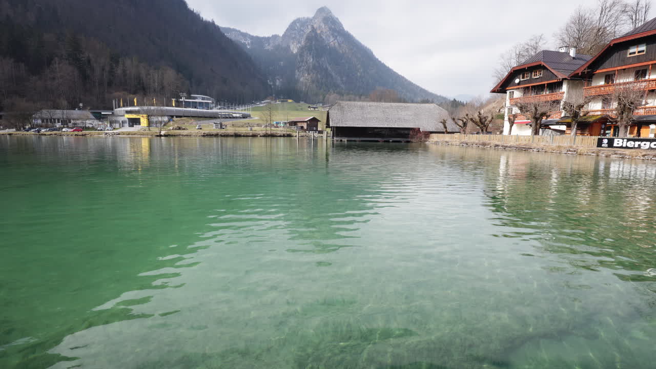 Serene view over the clear emerald waters of Königssee with traditional Bavarian houses and dramatic alpine peaks in the background
