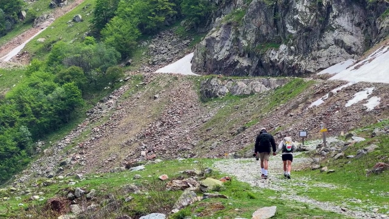 Un uomo e una donna camminano mano nella mano lungo un sentiero roccioso attraverso un paesaggio montano panoramico