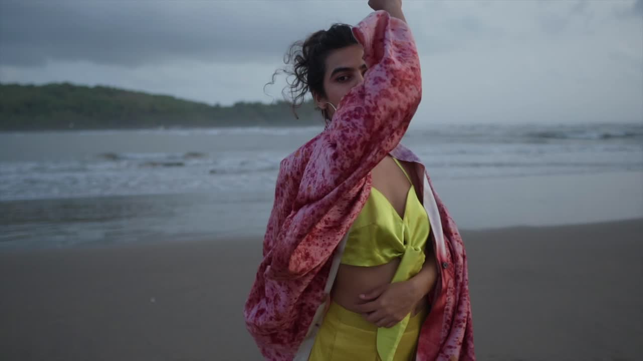 una hermosa chica posando en un colorido vestido de seda que flota en el viento en una playa de arena en el fondo