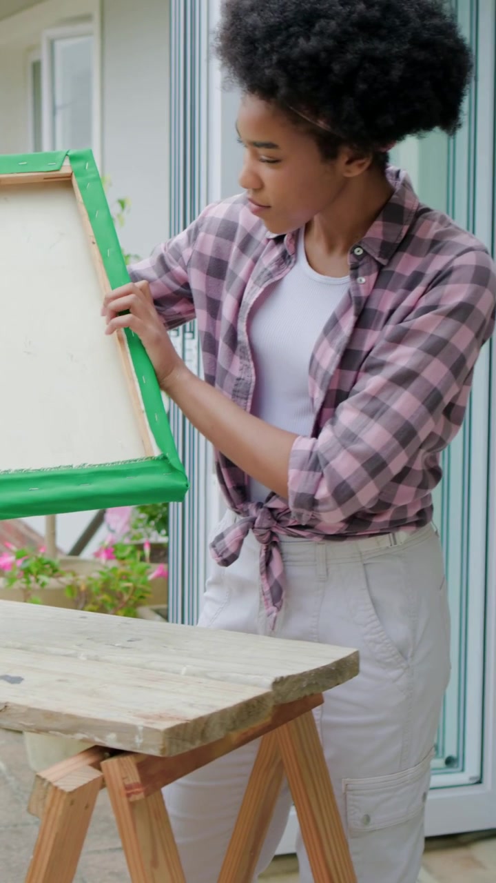 Video verticale: Donna che posiziona una cornice sul patio e liscia un tessuto verde per una tela, con una fascia rosa.