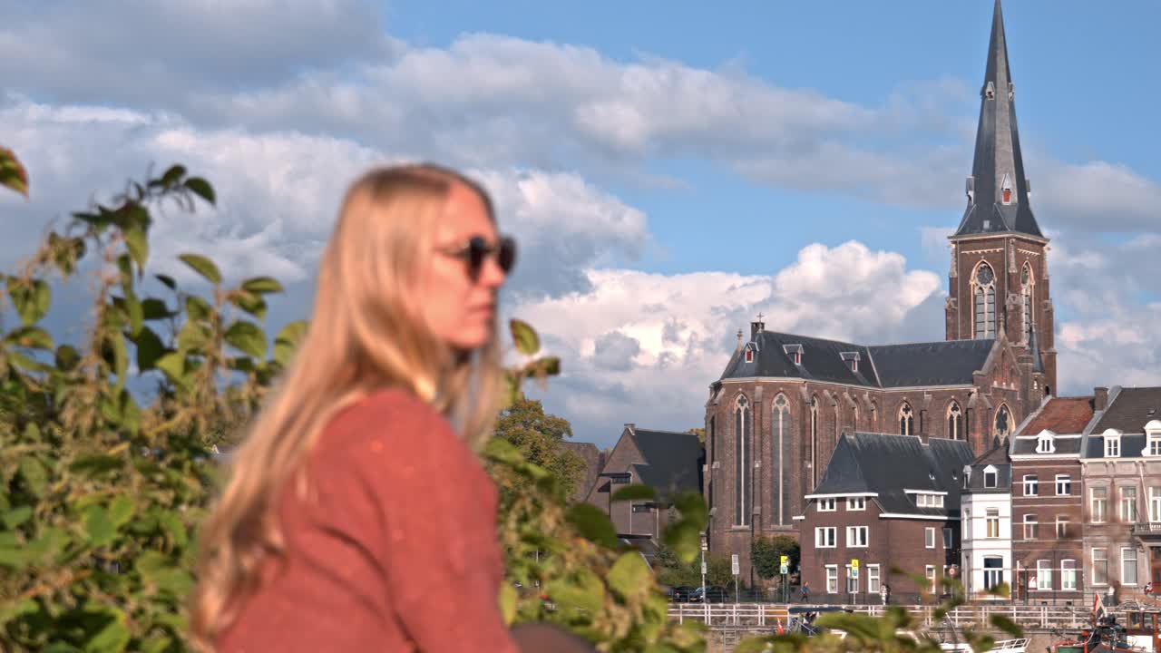 Woman standing on the riverbank in Maastricht, Netherlands, with the striking Sint-Martinuskerk (St. Martin's Church) as a prominent feature in the background
