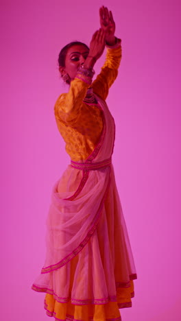 vertical video studio shot of female kathak dancer performing dance wearing traditional indian dress against purple background