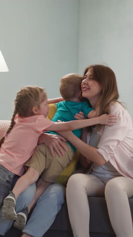 joyful little children sister and brother cuddle mother and granny in living room. happy women embrace adorable kids at home. positive emotions in family life