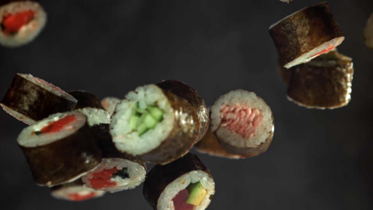 Deliziosi roll di sushi che fluttuano al rallentatore su uno sfondo scuro