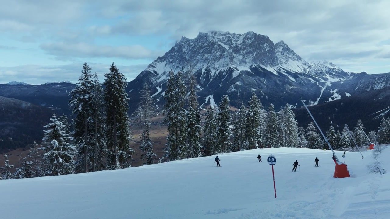 Sciatori che scendono un pendio innevato con cime montuose e foresta invernale intorno. Scattato con uno smartphone