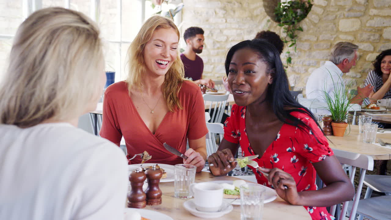 Three young adult women having brunch together and talking in a small restaurant, waist up