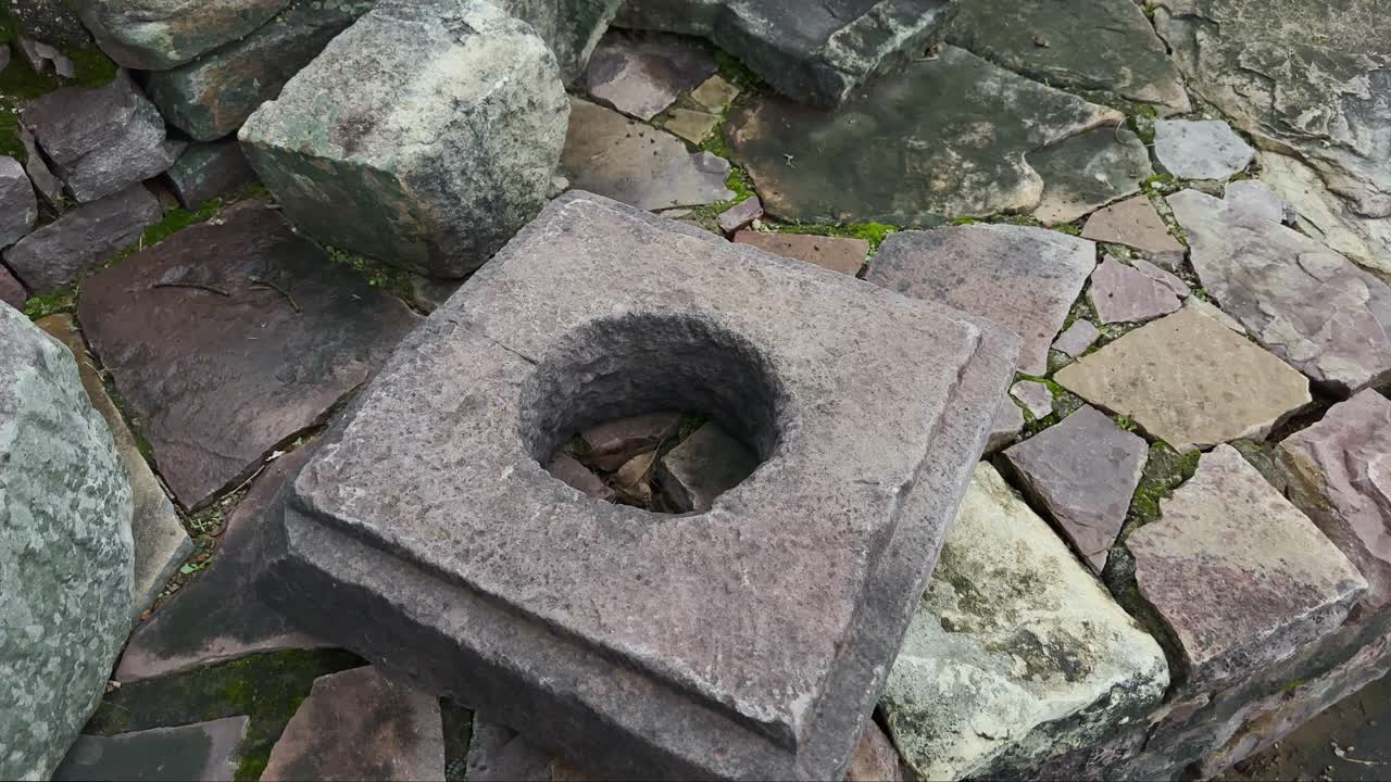 Древний резной каменный блок с круглым отверстием, окруженный выветренными каменными руинами, снятый с плавным круговым движением камеры, чтобы выделить историческую архитектуру и текстуры