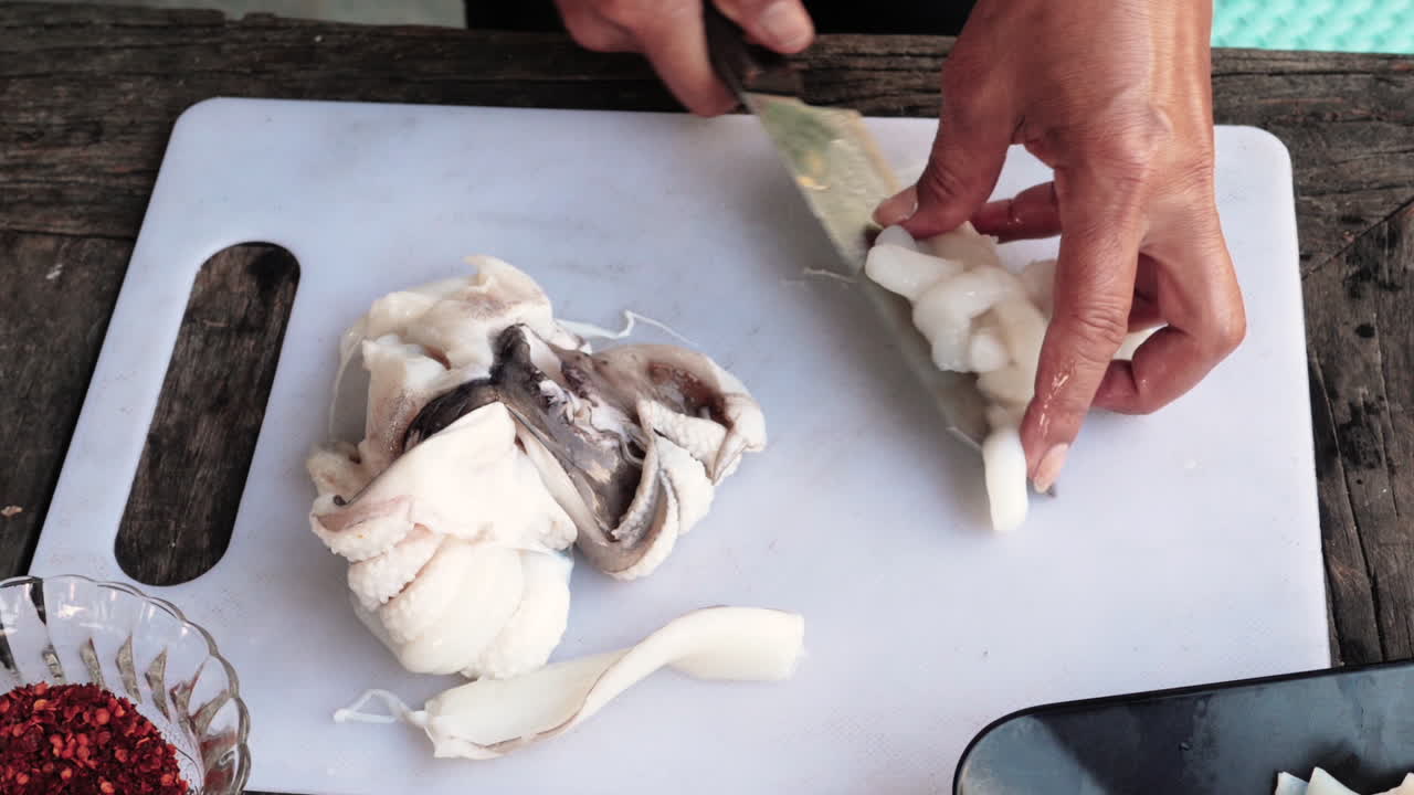 Close up shot woman cutting squid carefully on a white board - Food preparation