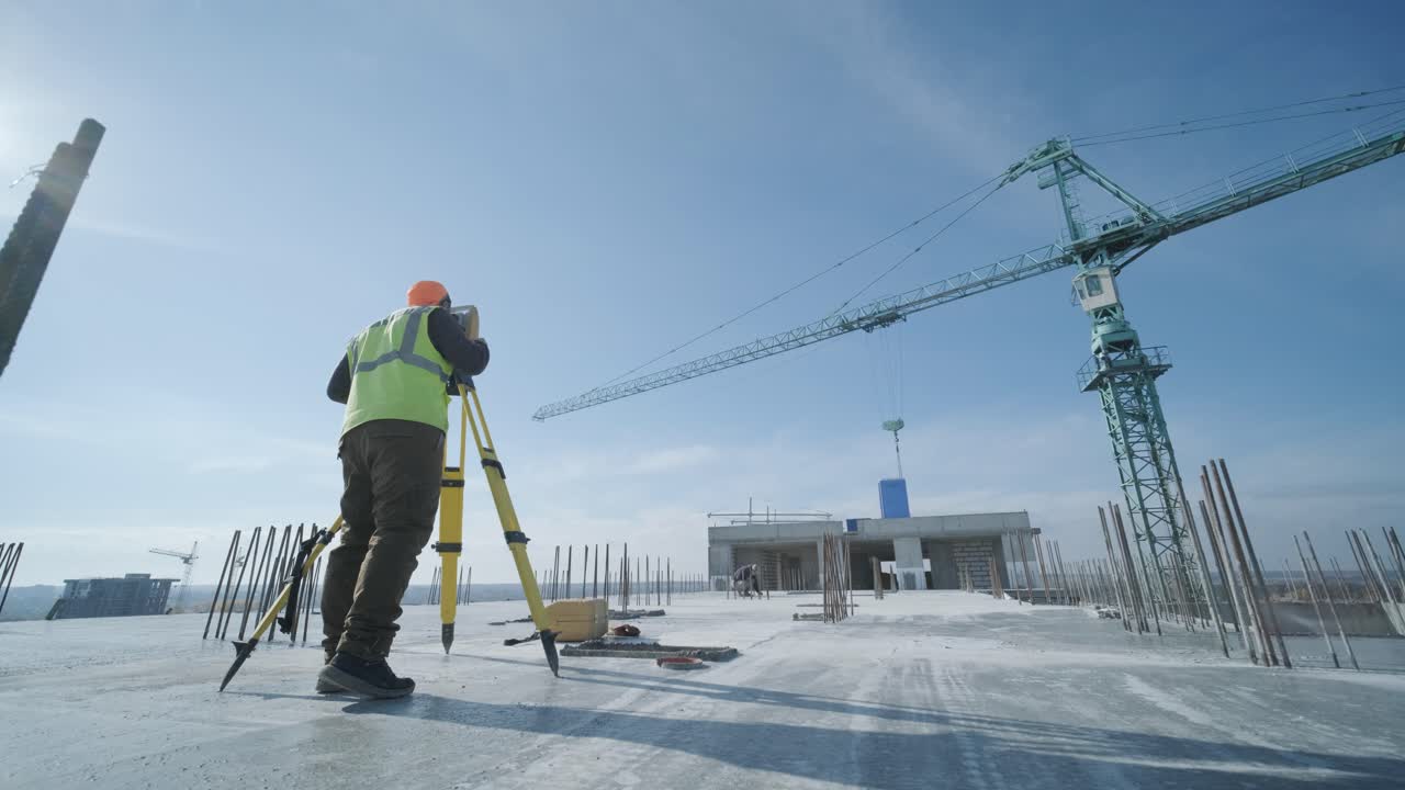 Geodetic works. Surveyor engineer in protective wear and red helmet using geodetic equipment at construction site. Professional equipment.