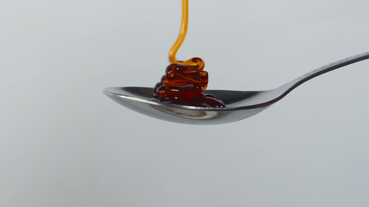 Sweet golden honey dripping, healthy liquid nectar flowing onto a metal spoon and dropping down