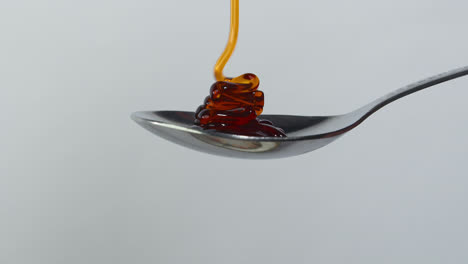 sweet golden honey dripping, healthy liquid nectar flowing onto a metal spoon and dropping down