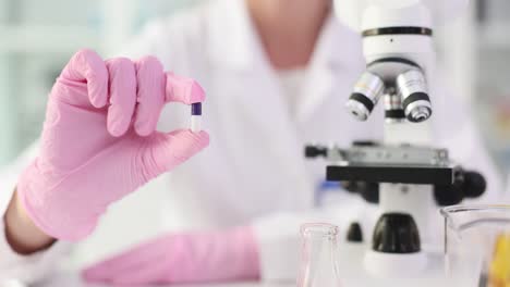 scientist in pink gloves holding a pill in a laboratory with a microscope