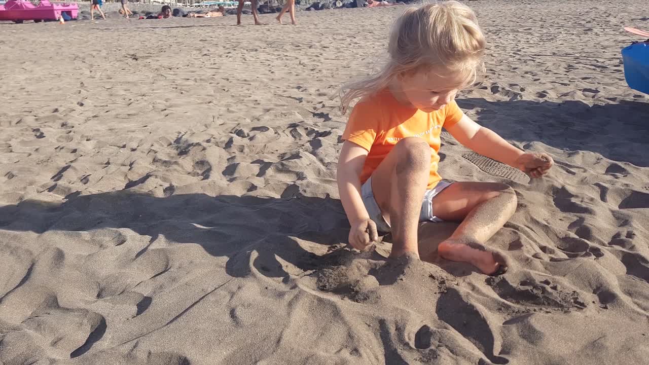 Child sitting throwing sand from the beach on top of it