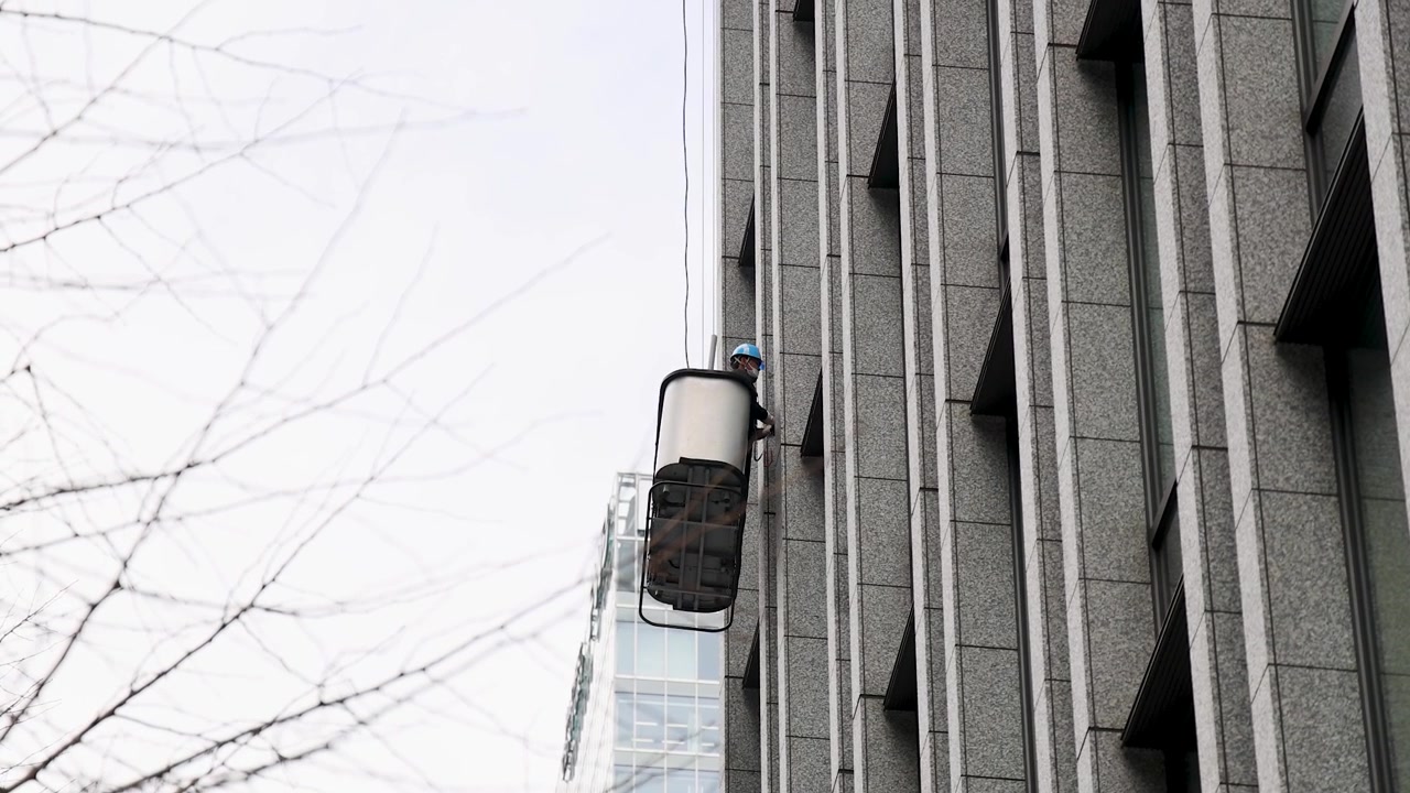 Un tecnico su una piattaforma elevatrice di sicurezza pulisce le finestre di un moderno grattacielo a Tokyo, Giappone