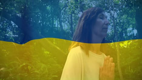 Animation-of-flag-of-ukraine-over-caucasian-woman-praying-outdoors