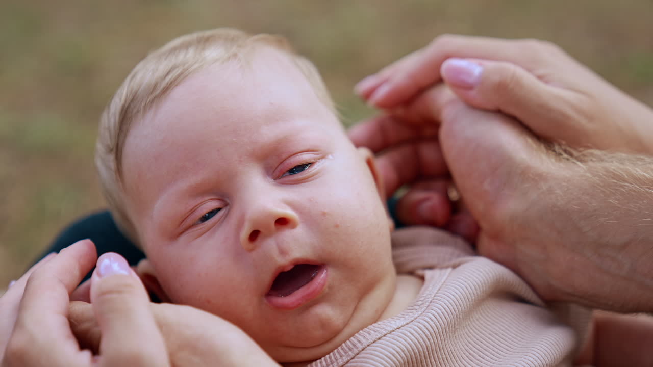 Face of an adorable infant baby two month old. Hands of parents touch the eras of a blue-eyed child. Close up.