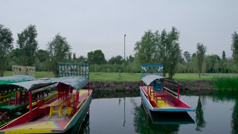 Dolly-out-in-middle-of-trajineras-above-a-lake-and-natural-area-with-view-of-a-trail-in-Xochimilco,-Mexico-City