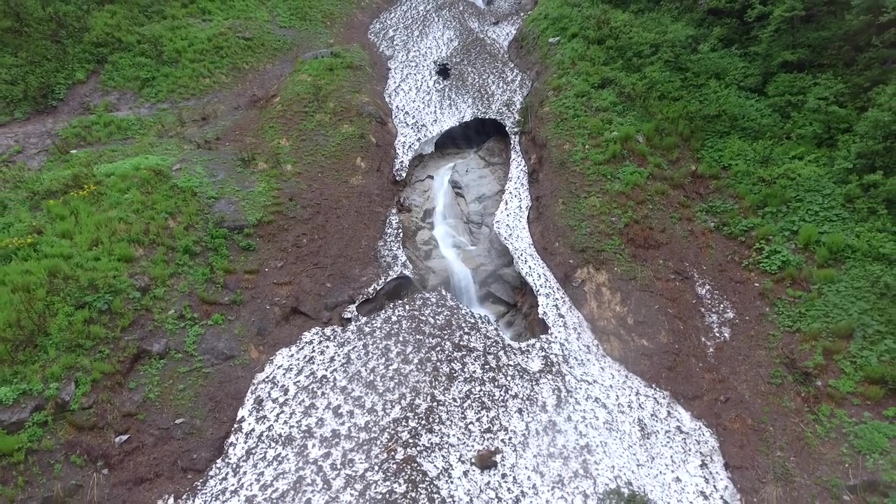 Vista aerea di una cascata che scorre tra la neve sciolta in montagna