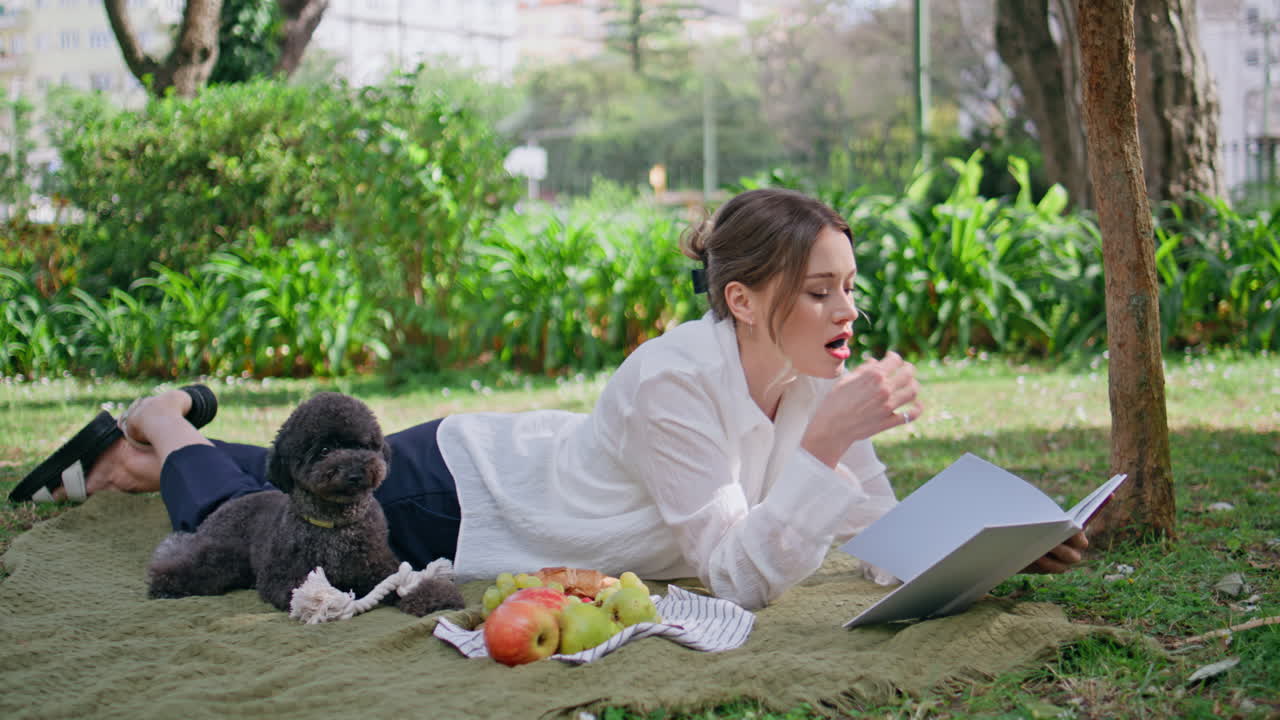 Girl reading book nature lying blanket with little dog. Smiling woman at picnic