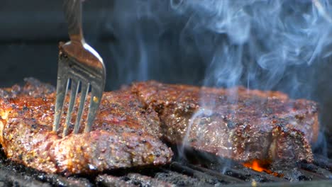 A-fork-turns-a-nearly-cooked-juicy-rib-eye-steak-on-a-grill