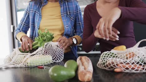 Midsection-of-biracial-lesbian-couple-unpacking-grocery-shopping-bags-in-kitchen,-in-slow-motion