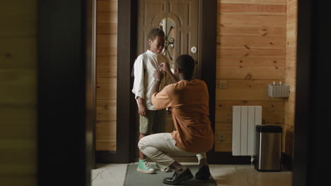 loving dad helping his son to fasten buttons on his shirt, then opening the door and the boy leaving home