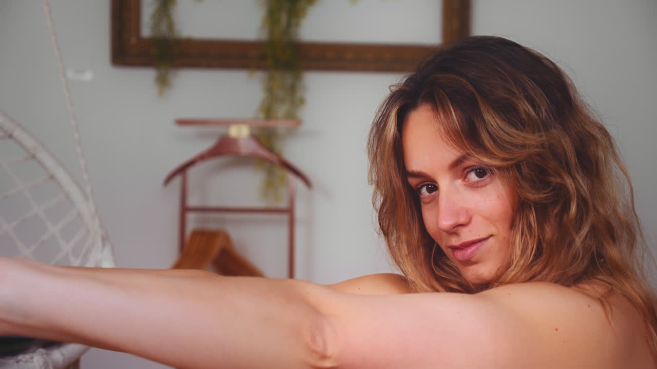 행복한 미소로 카메라를 바라보며 아늑한 집에서 요가를 하는 아름다운 여성