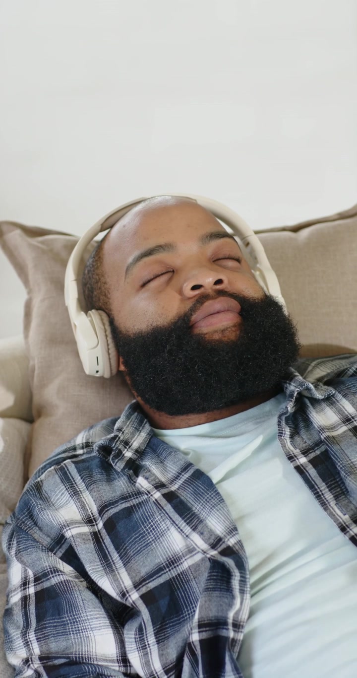 Vertical video: African American man at home reclining in plaid listening on headphones relaxing